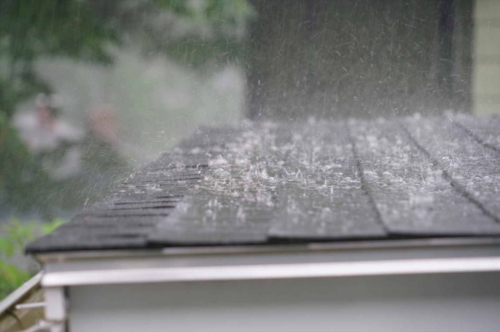 Heavy rain falling on an asphalt shingle roof, with water splashing and blurring in motion.